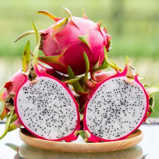 Dragon fruit with a cut open one showing its interior on a wooden plate.
