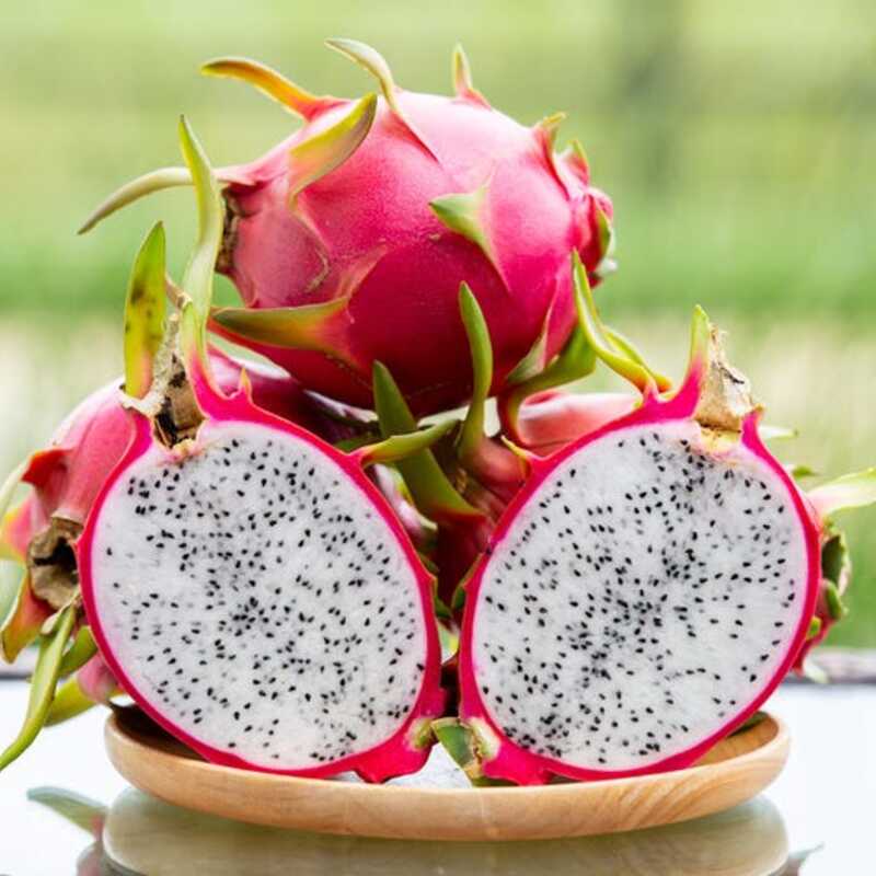 Dragon fruit with a cut open one showing its interior on a wooden plate.